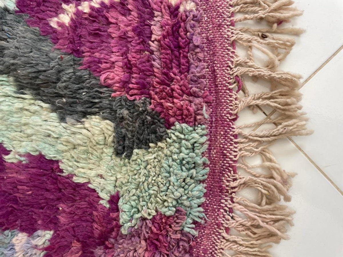 Close-up detail of a vintage Moroccan rug featuring handcrafted fringe edges in purple, green, and beige.