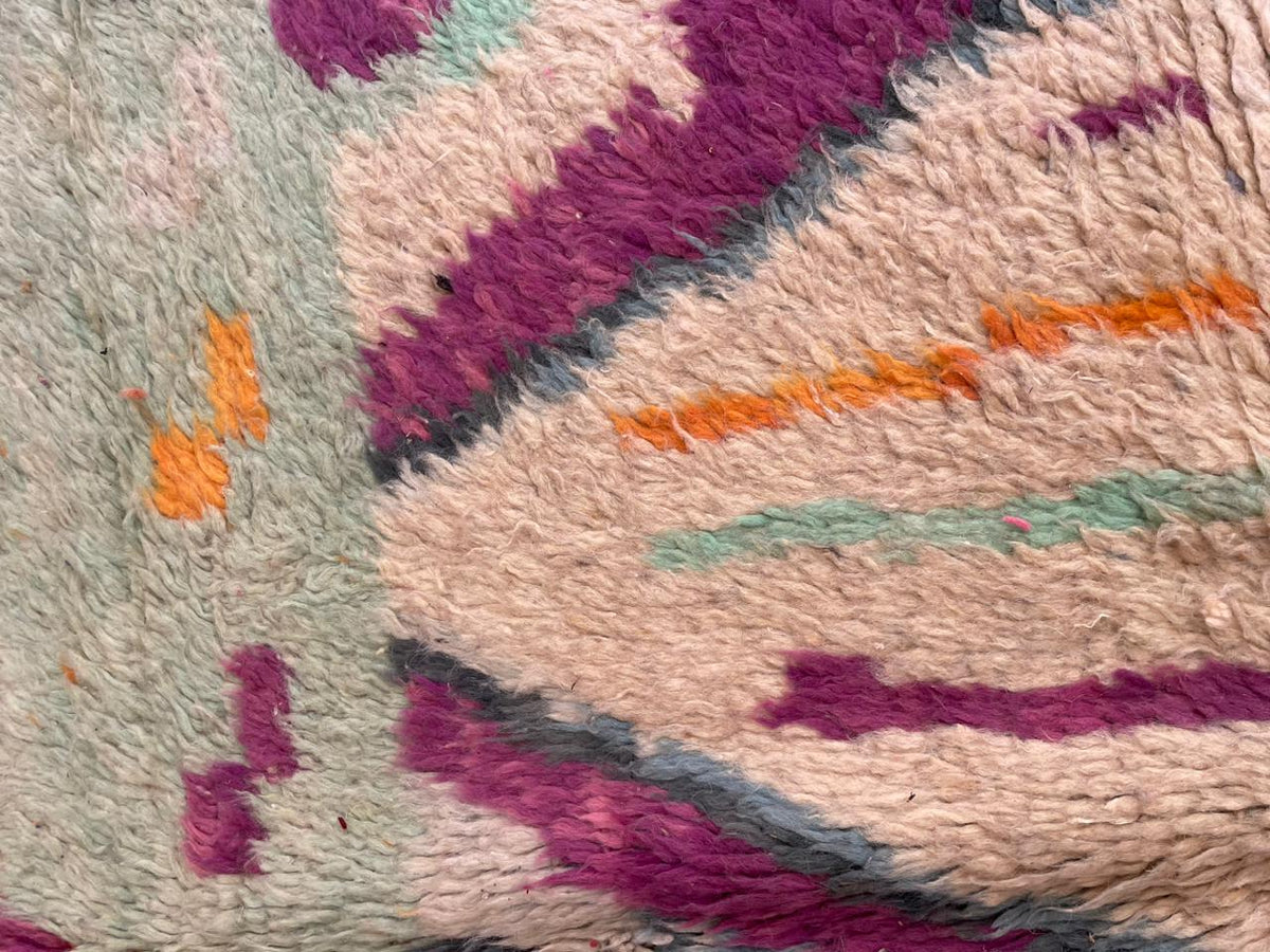 Close-up detail of a vintage Moroccan rug displaying abstract patterns in purple, orange, green, and cream.