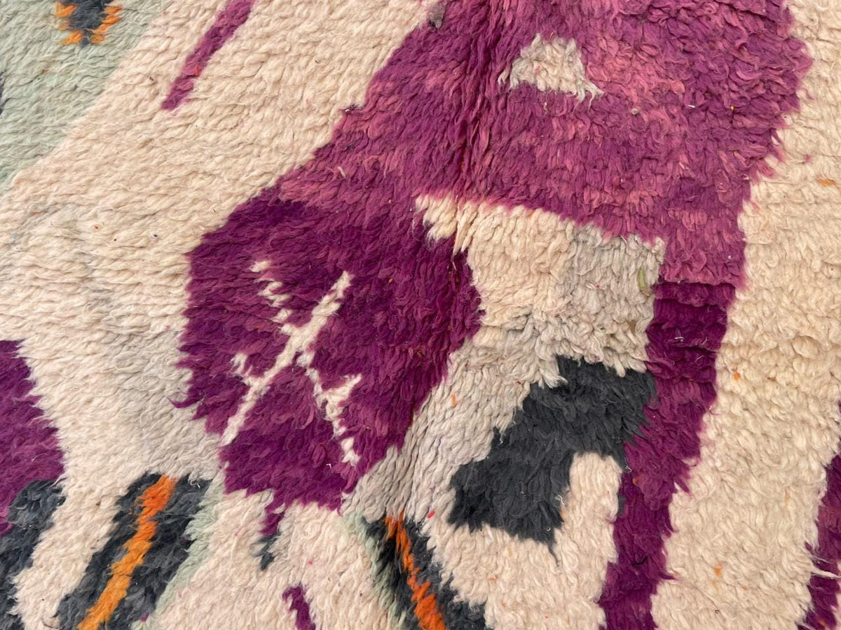 Close-up detail of a vintage Moroccan rug showcasing intricate patterns in purple, pink, black, and cream.
