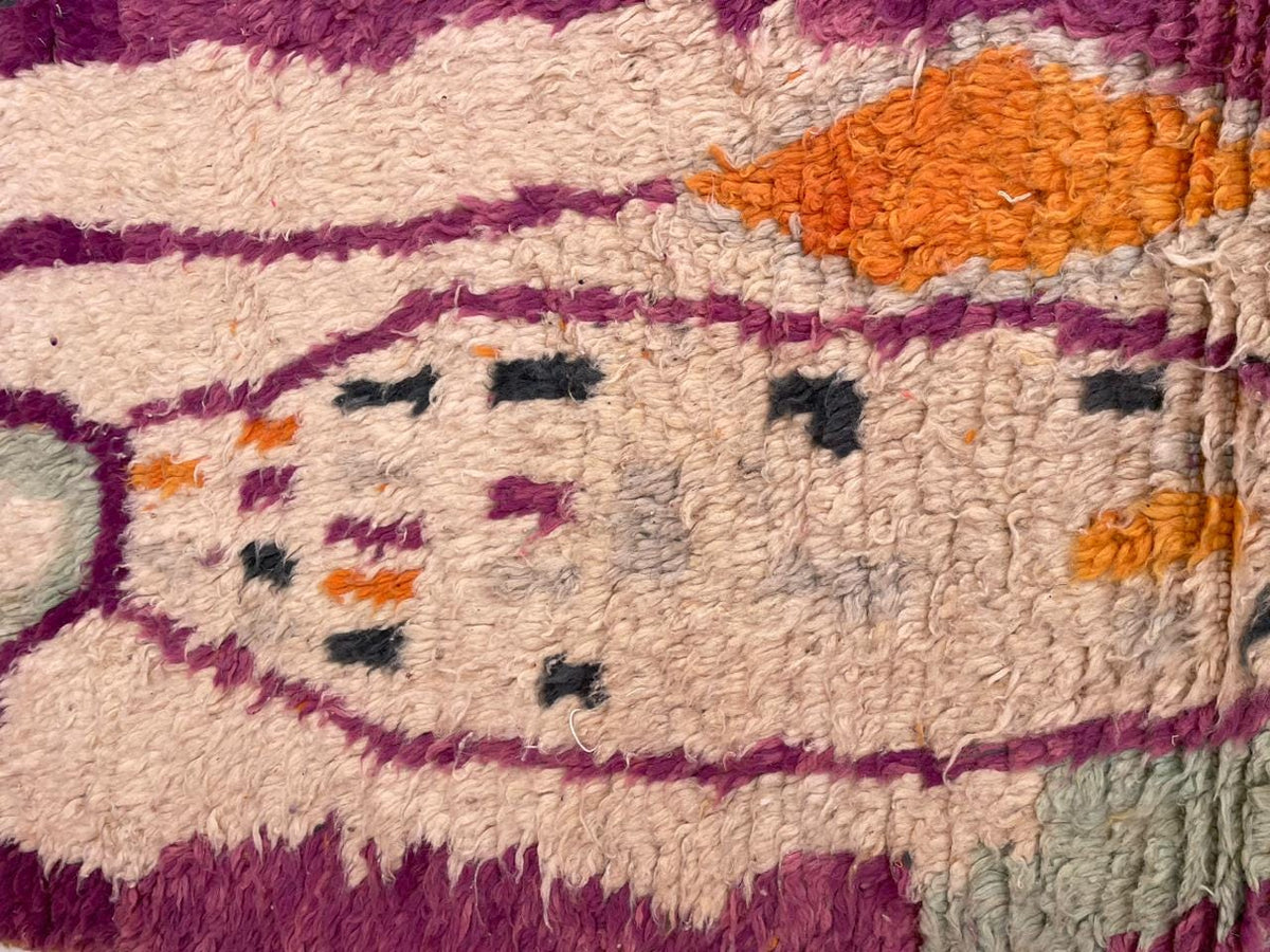 Close-up detail of a vintage Moroccan rug featuring geometric patterns in purple, orange, black, and cream.
