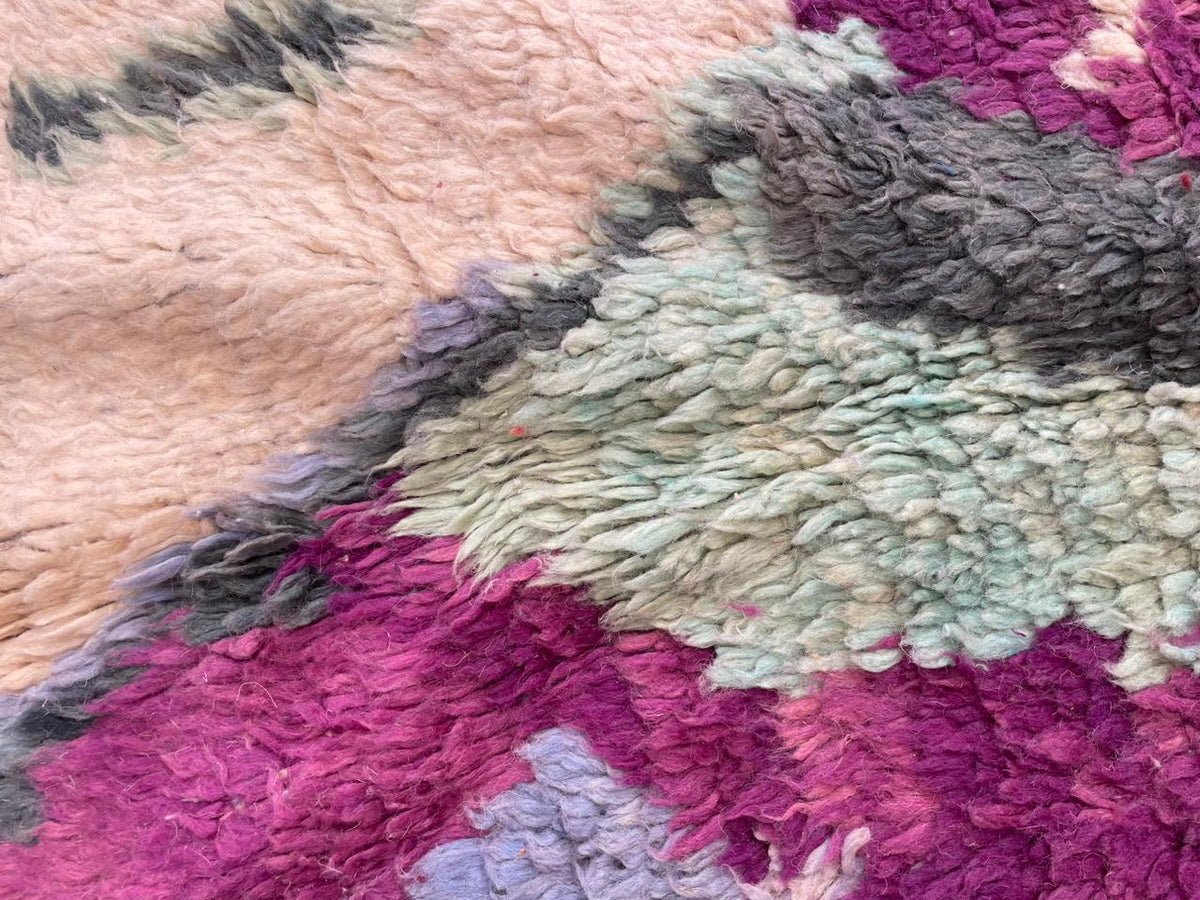 Close-up detail of a vintage Moroccan rug with a textured surface in purple, pink, green, and cream.