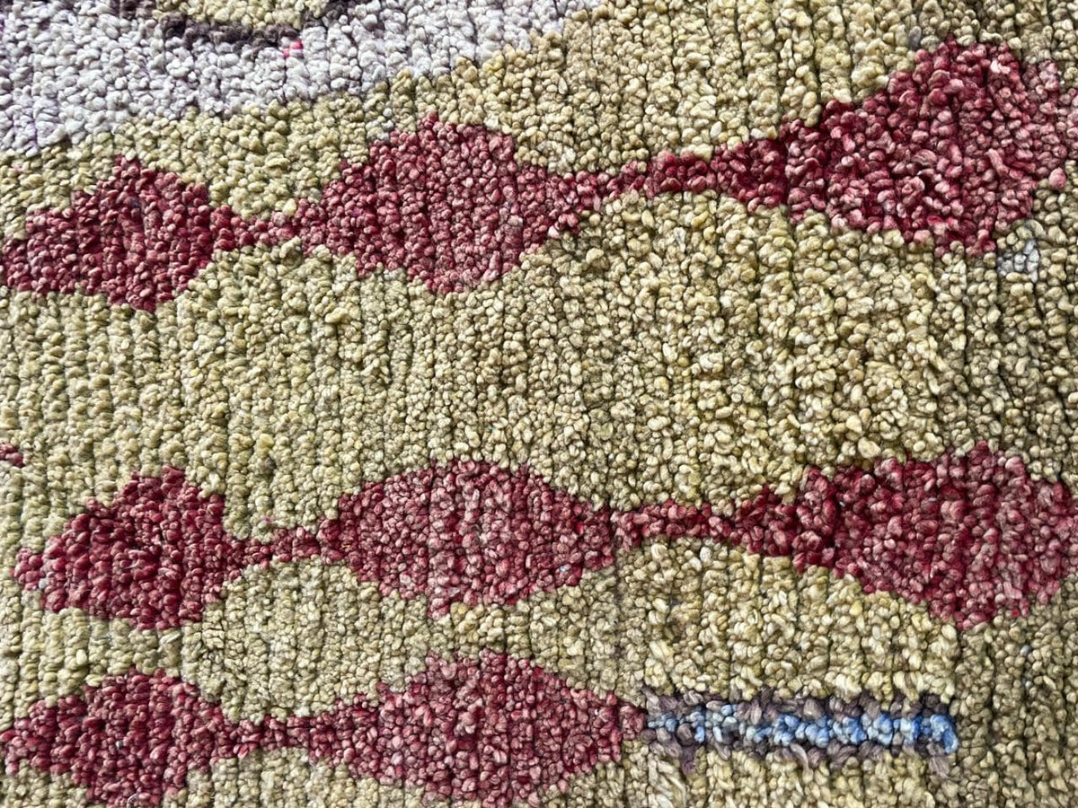 Detail shot of a vintage Moroccan rug highlighting a fish pattern and textured weave in yellow and red.