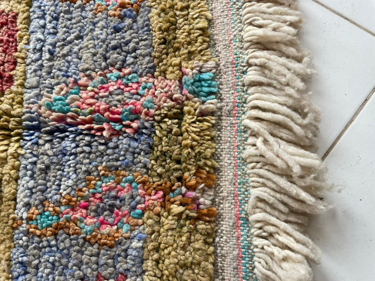Close-up detail of a vintage Moroccan rug with fringe edges and colorful accents in beige, blue, and orange.