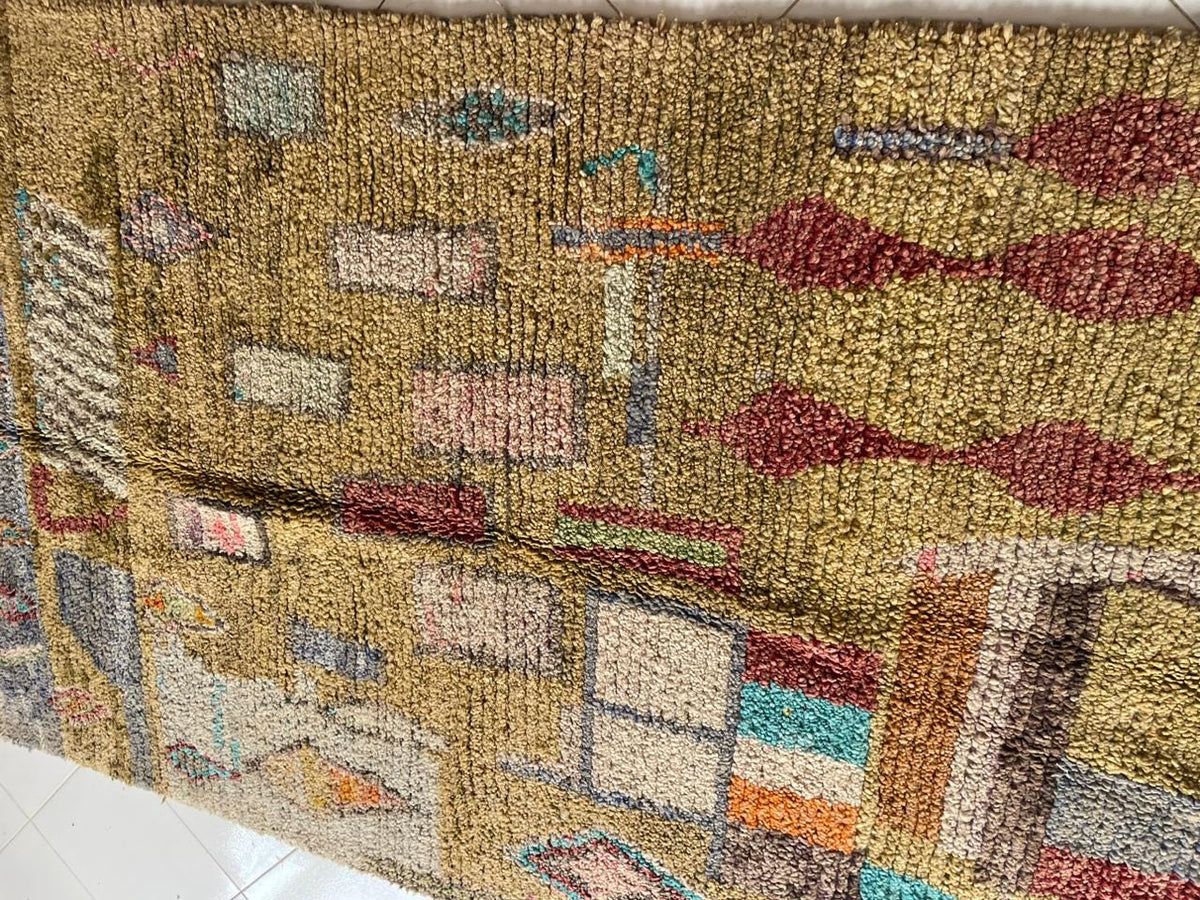 Side view of a vintage Moroccan rug displaying geometric patterns and a textured surface in gold, red, and blue.