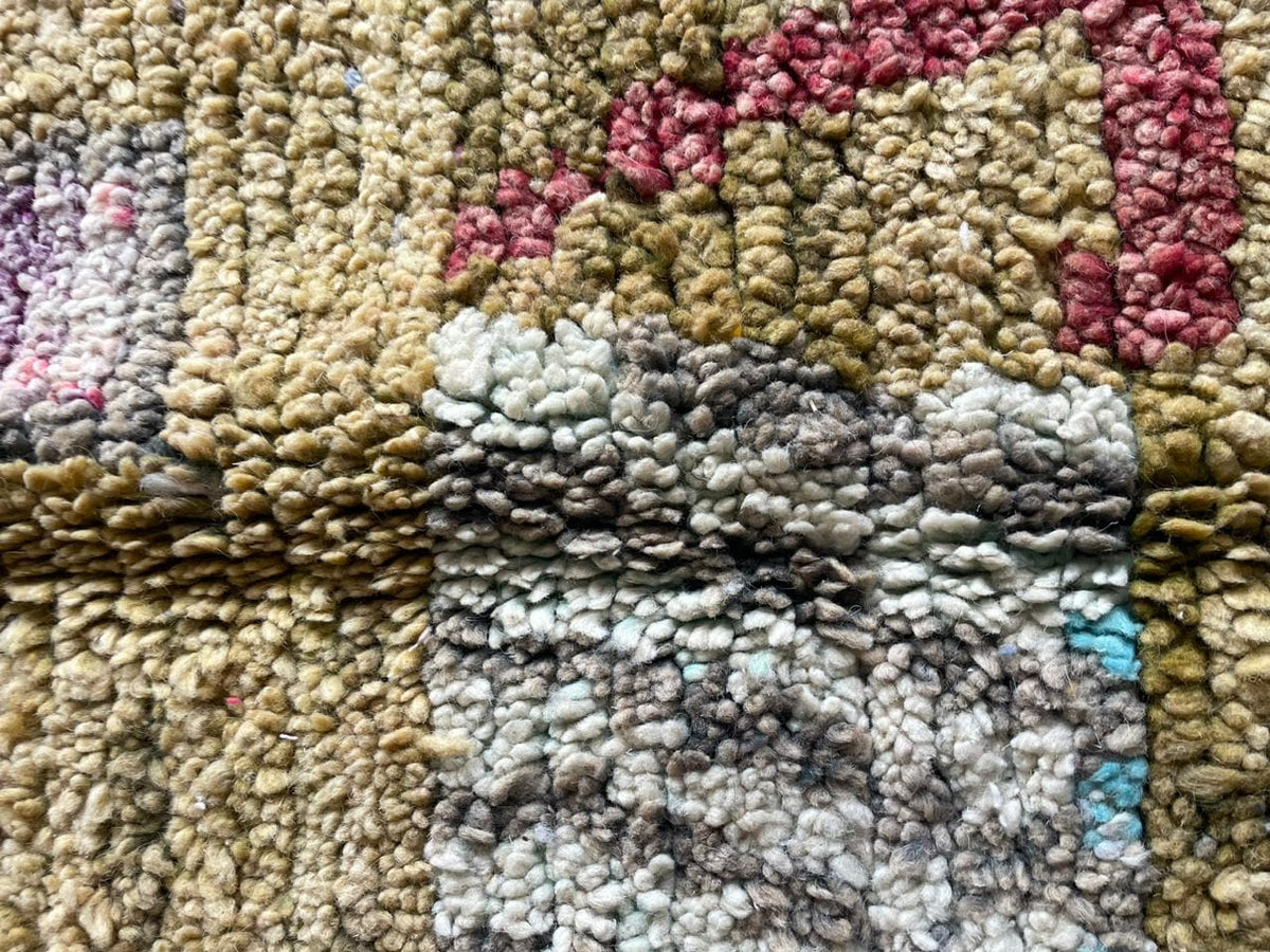 Detail shot of a vintage Moroccan rug with patchwork style and soft fibers in gold, red, and blue.