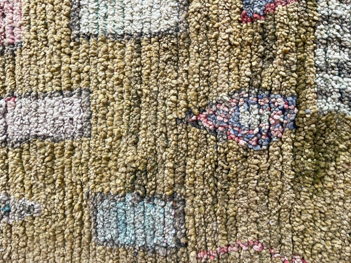 Close-up detail of a vintage Moroccan rug featuring geometric patterns and a textured surface in beige, blue, and pink.