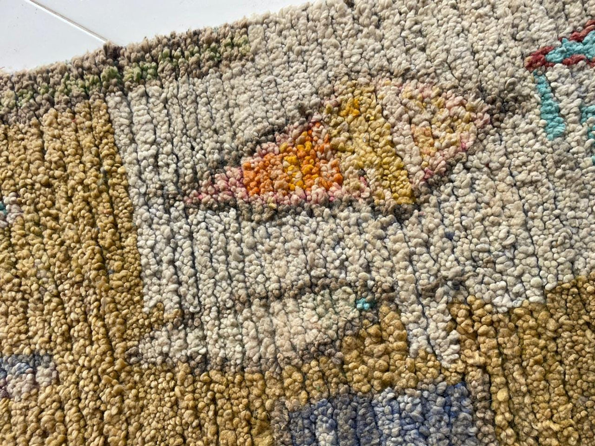 Close-up of a vintage Moroccan rug featuring an intricate design and woven texture in beige, orange, and blue.