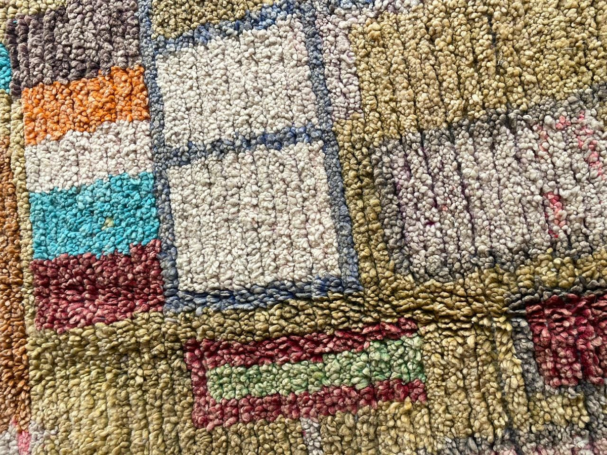 Close-up detail of a vintage Moroccan rug showcasing colorful squares and a textured weave in yellow, red, and blue.