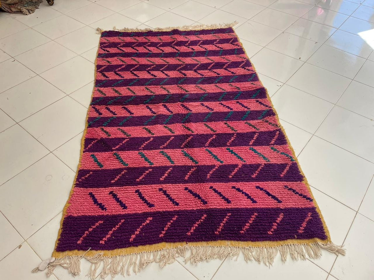 Front view of a pink vintage Moroccan rug featuring fringed edges and a solid background.