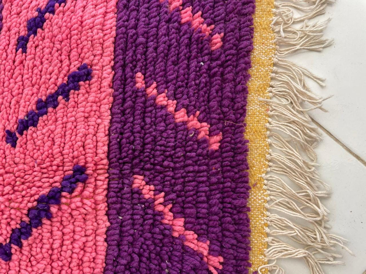 Detail view of a pink wool rug featuring geometric patterns and a fringe edge.