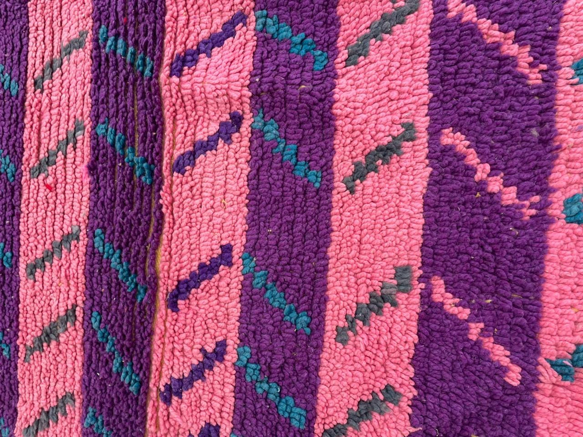 Top view of a pink vintage Moroccan rug showcasing a geometric design and fringed edges.