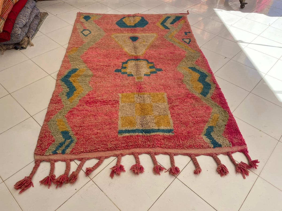 Front view of a vintage Moroccan rug with decorative patterns in pink, blue, and yellow.