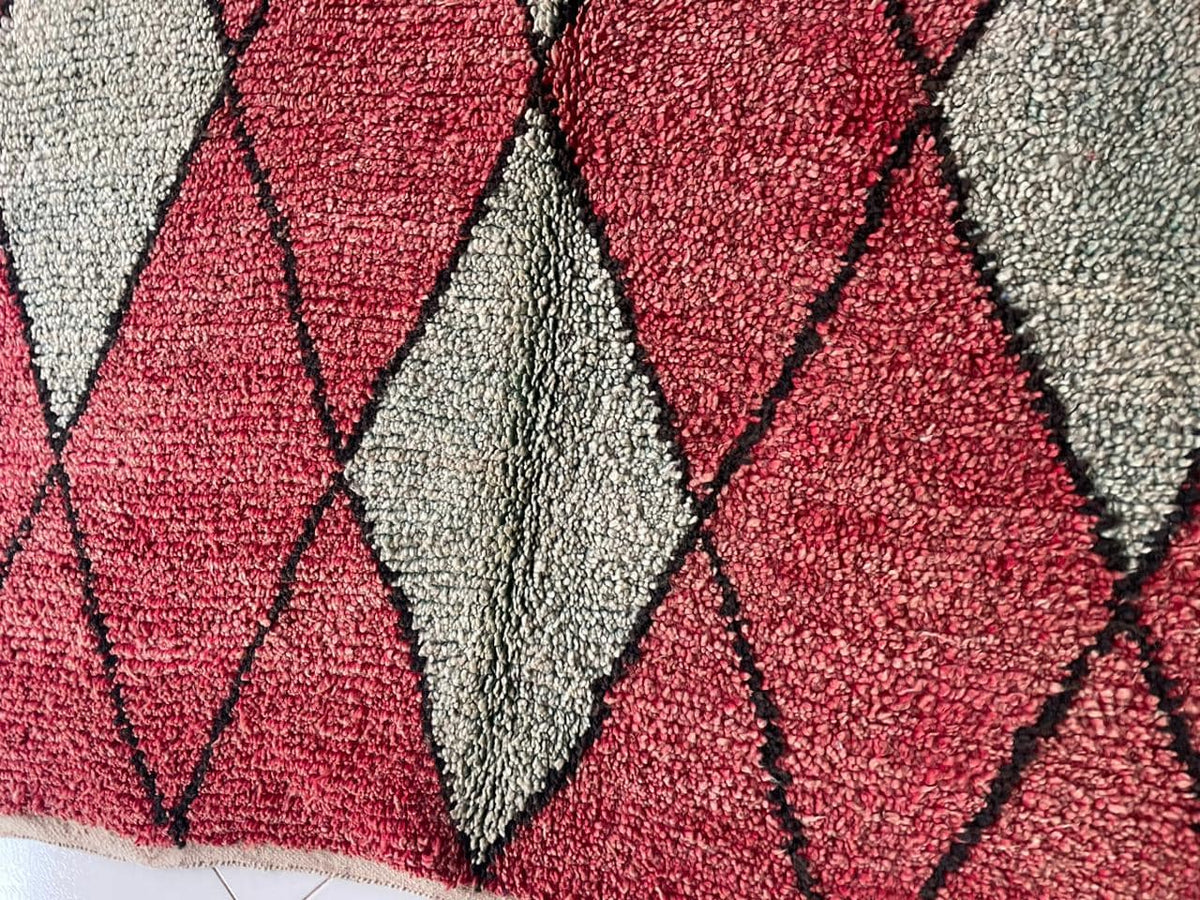 Detail close-up of a Moroccan rug with a diamond pattern in red, gray, and black.