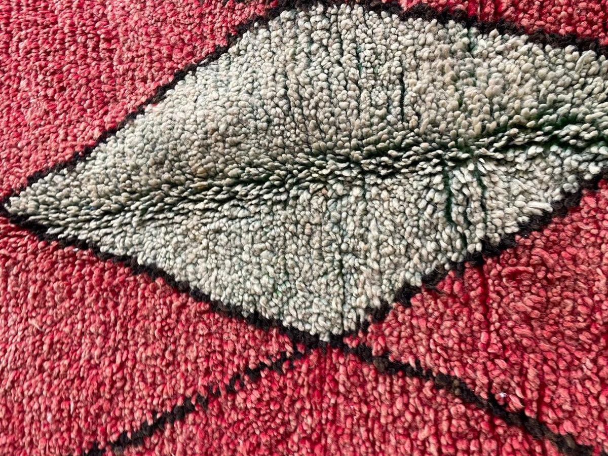 Detail close-up of the textured surface of a red Moroccan rug highlighting the diamond pattern.