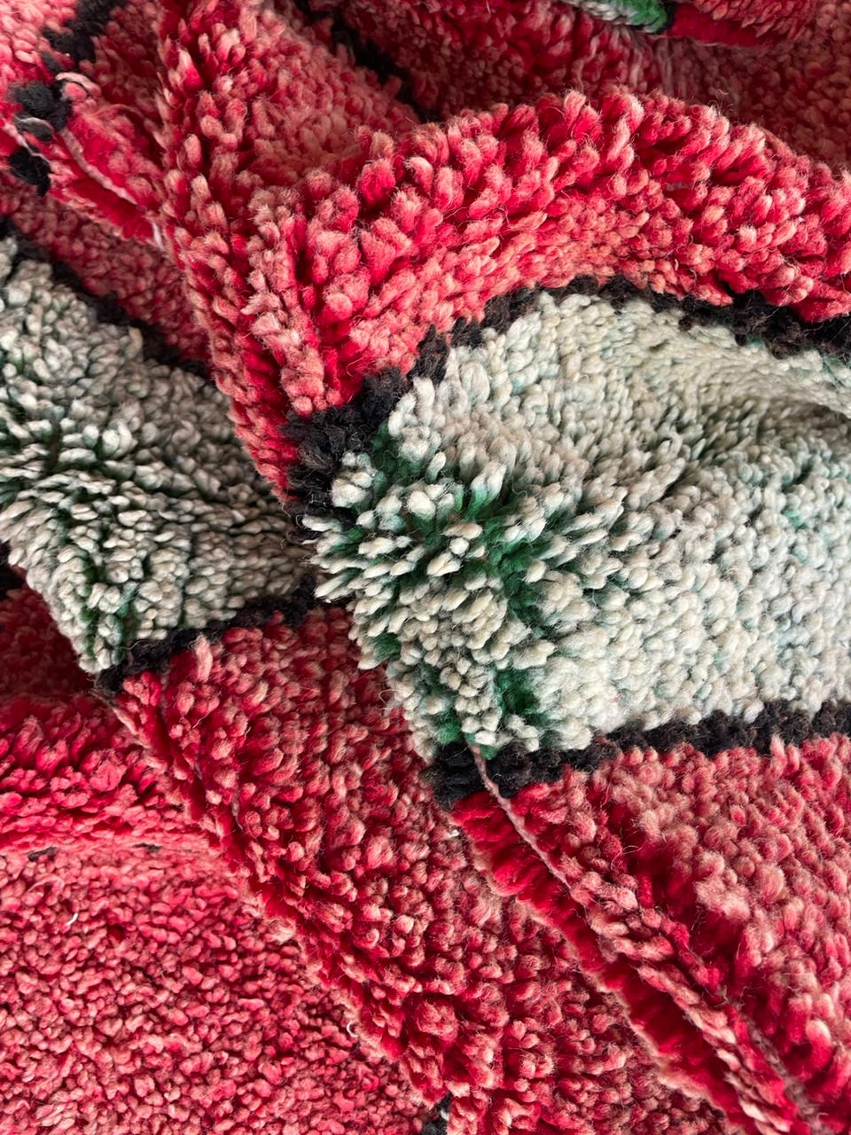 Detail close-up of a Moroccan rug featuring an intricate design in red, gray, and green.