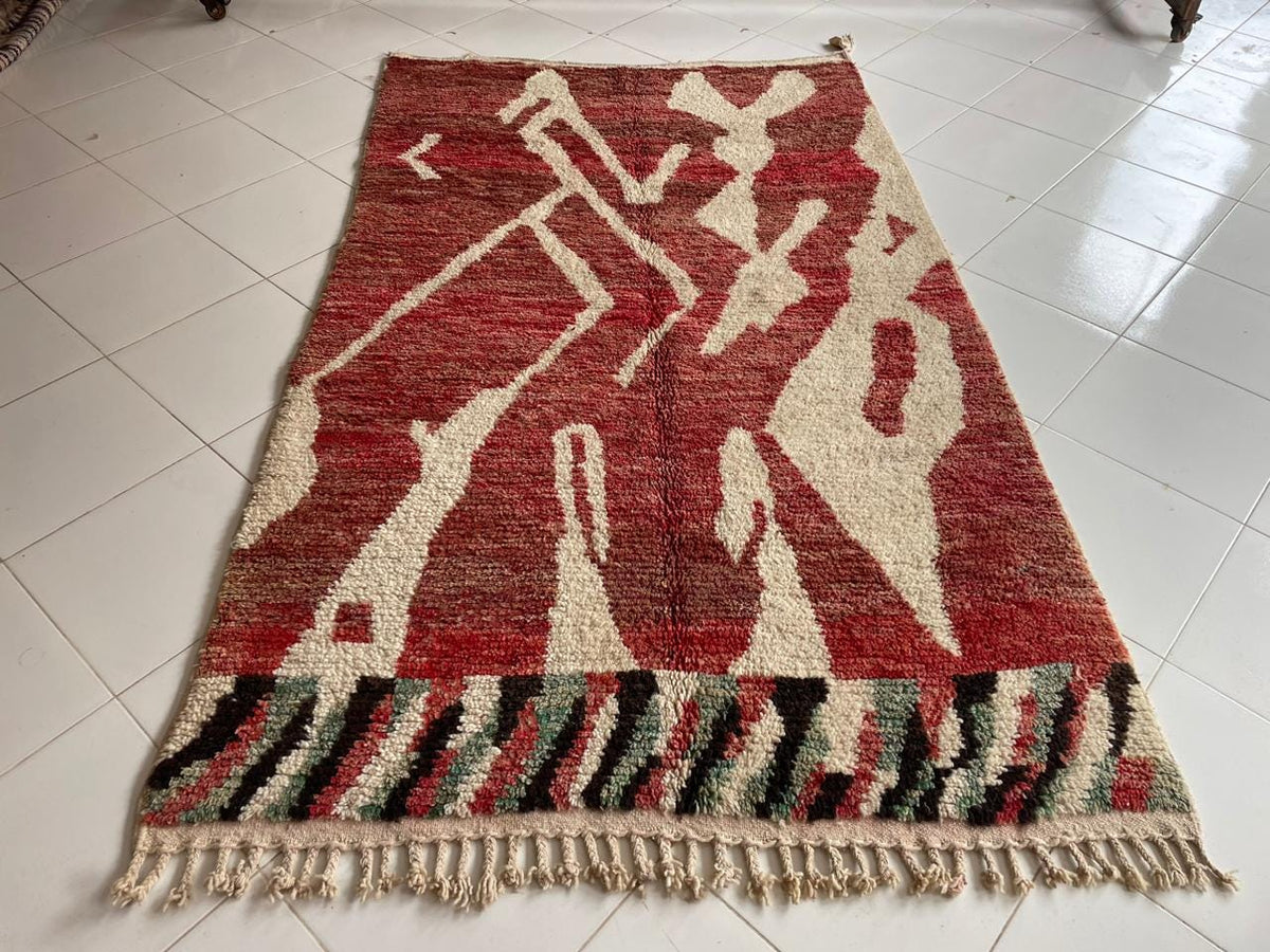 Top view of a red Moroccan rug featuring fringed edges and a bold design.