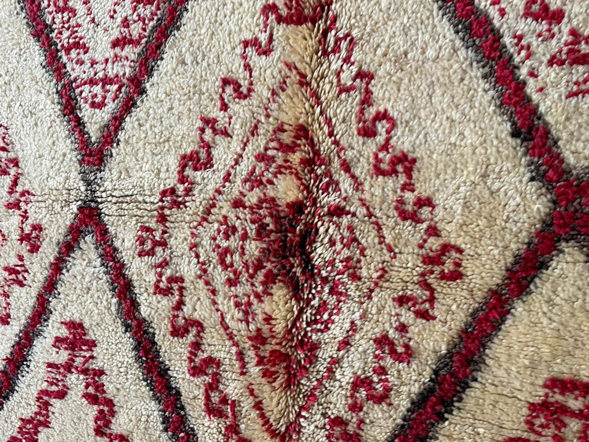 Detail view of a red Moroccan rug with diamond patterns and intricate design.