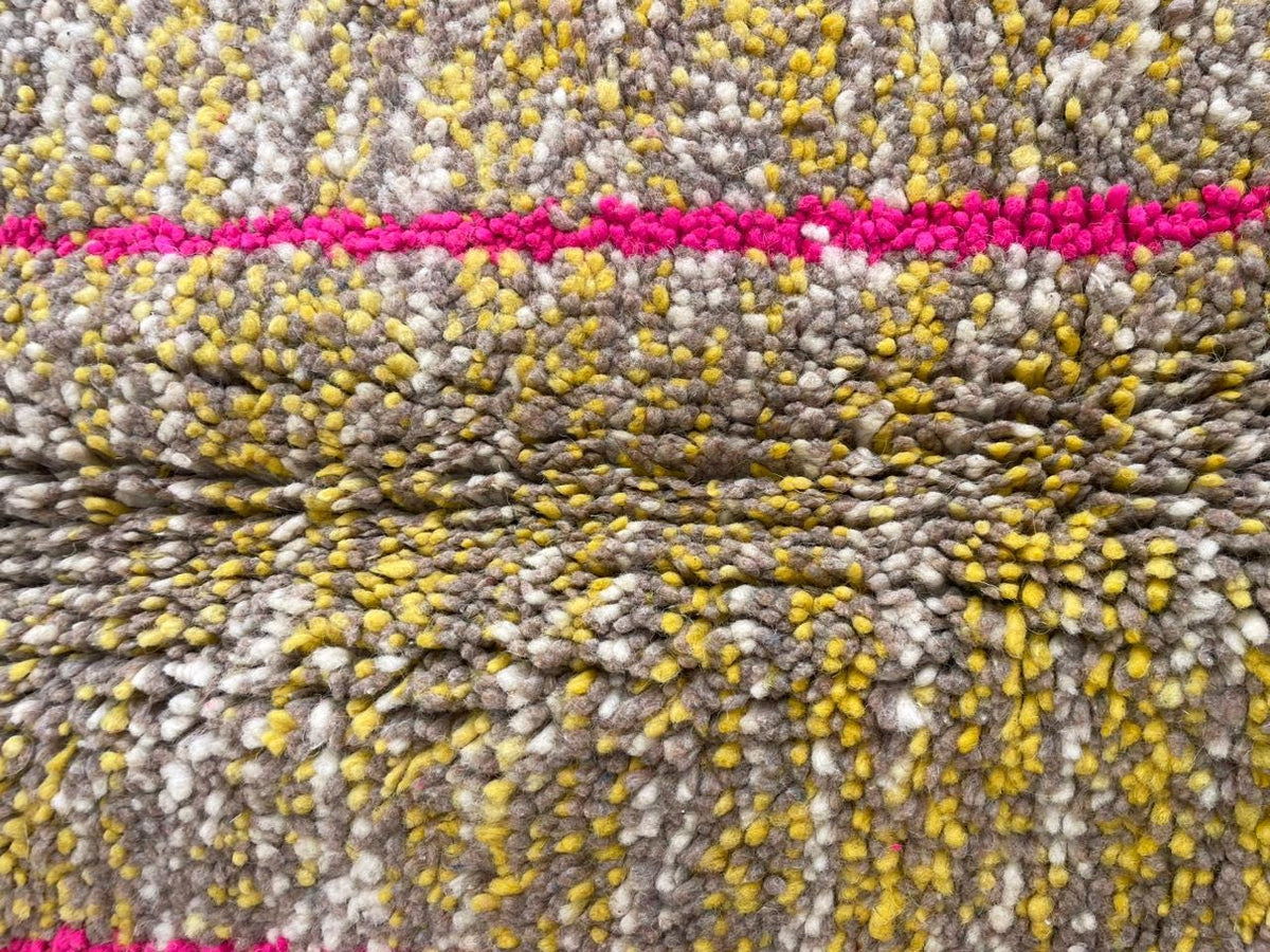 Detail close-up of a vintage Moroccan rug featuring a textured weave and geometric patterns in yellow, pink, and gray.