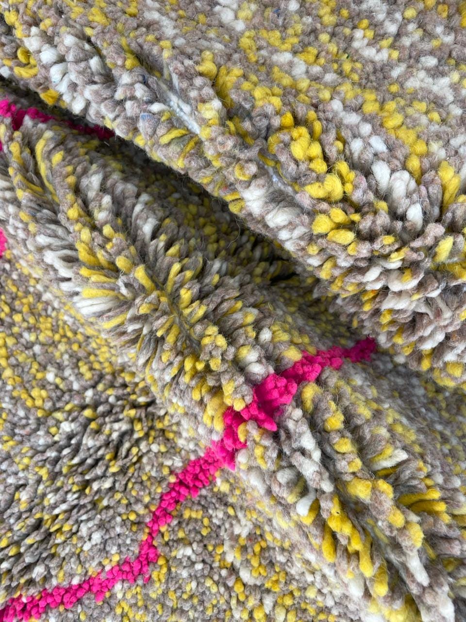 Detail close-up of a vintage Moroccan rug displaying a woven texture and colorful patterns in yellow, gray, and pink.