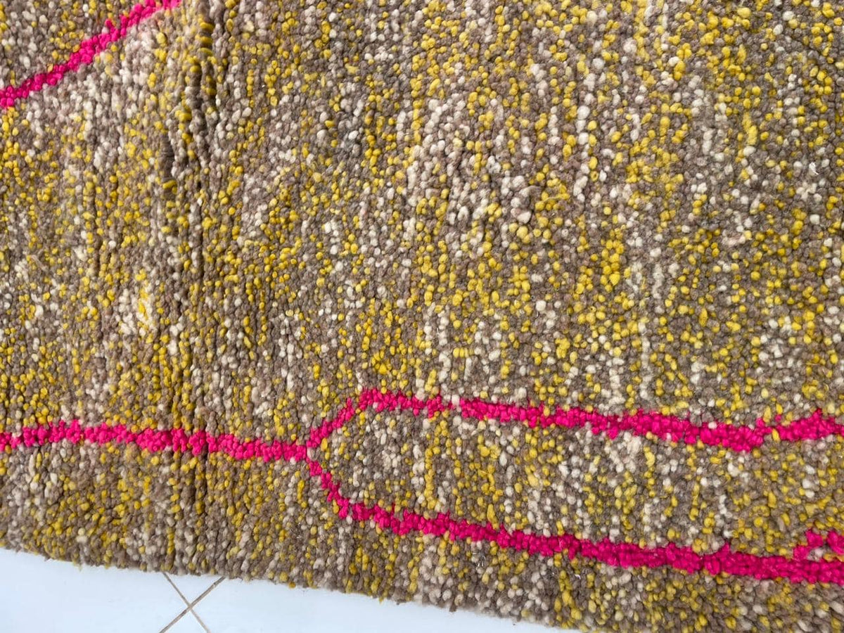 Detail close-up of a vintage Moroccan rug with a textured weave and geometric patterns in yellow, pink, and gray.