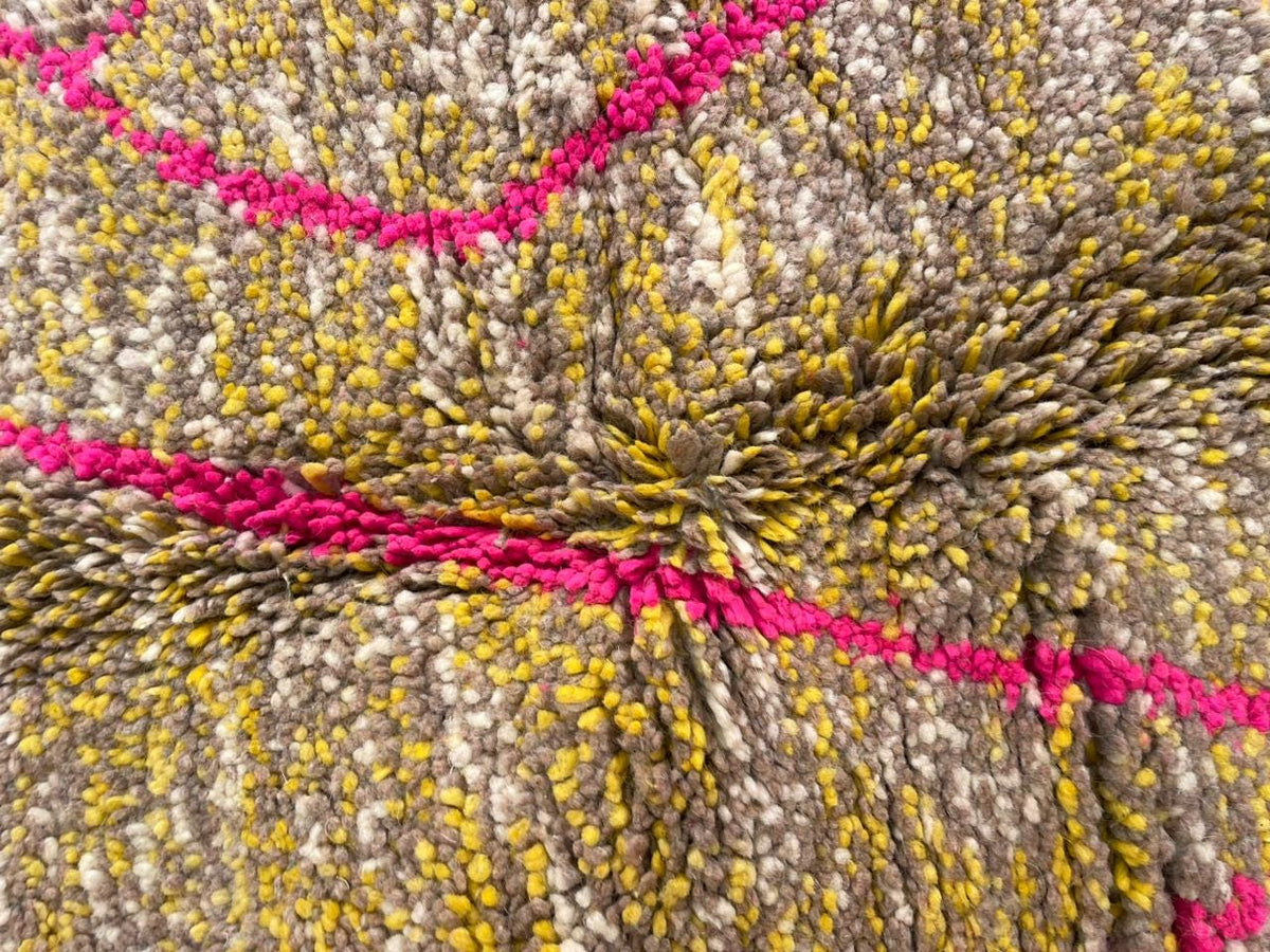 Detail close-up of a vintage Moroccan rug showcasing a textured weave and geometric patterns in yellow, pink, and gray.
