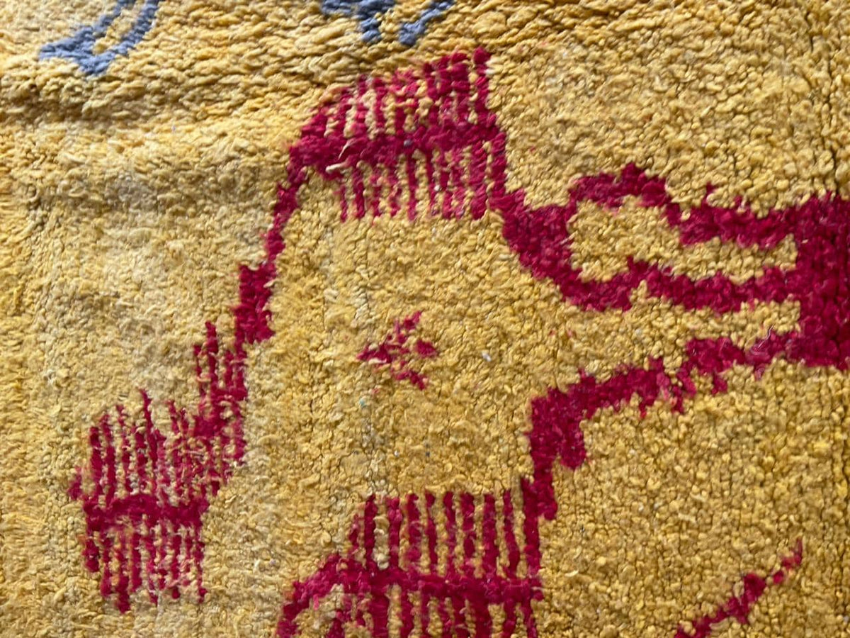 Close-up detail of a yellow Moroccan rug with abstract patterns and a textured surface.