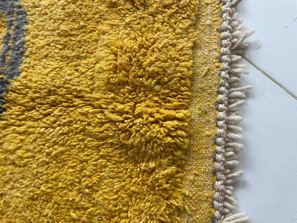 Close-up detail of a yellow Moroccan rug with a textured surface and decorative fringe.