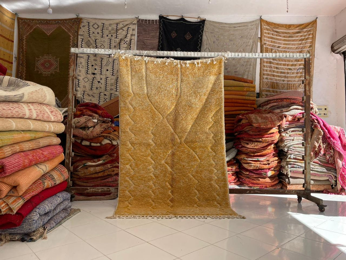 Lifestyle shot of a yellow rug displayed with various other rugs in a studio background.