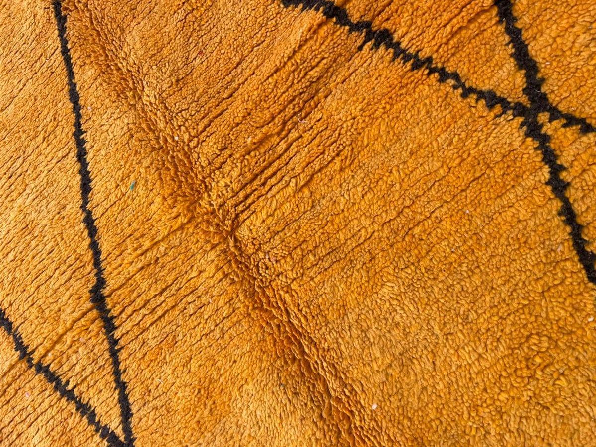 Detail view of a yellow wool rug featuring an abstract design and smooth surface.