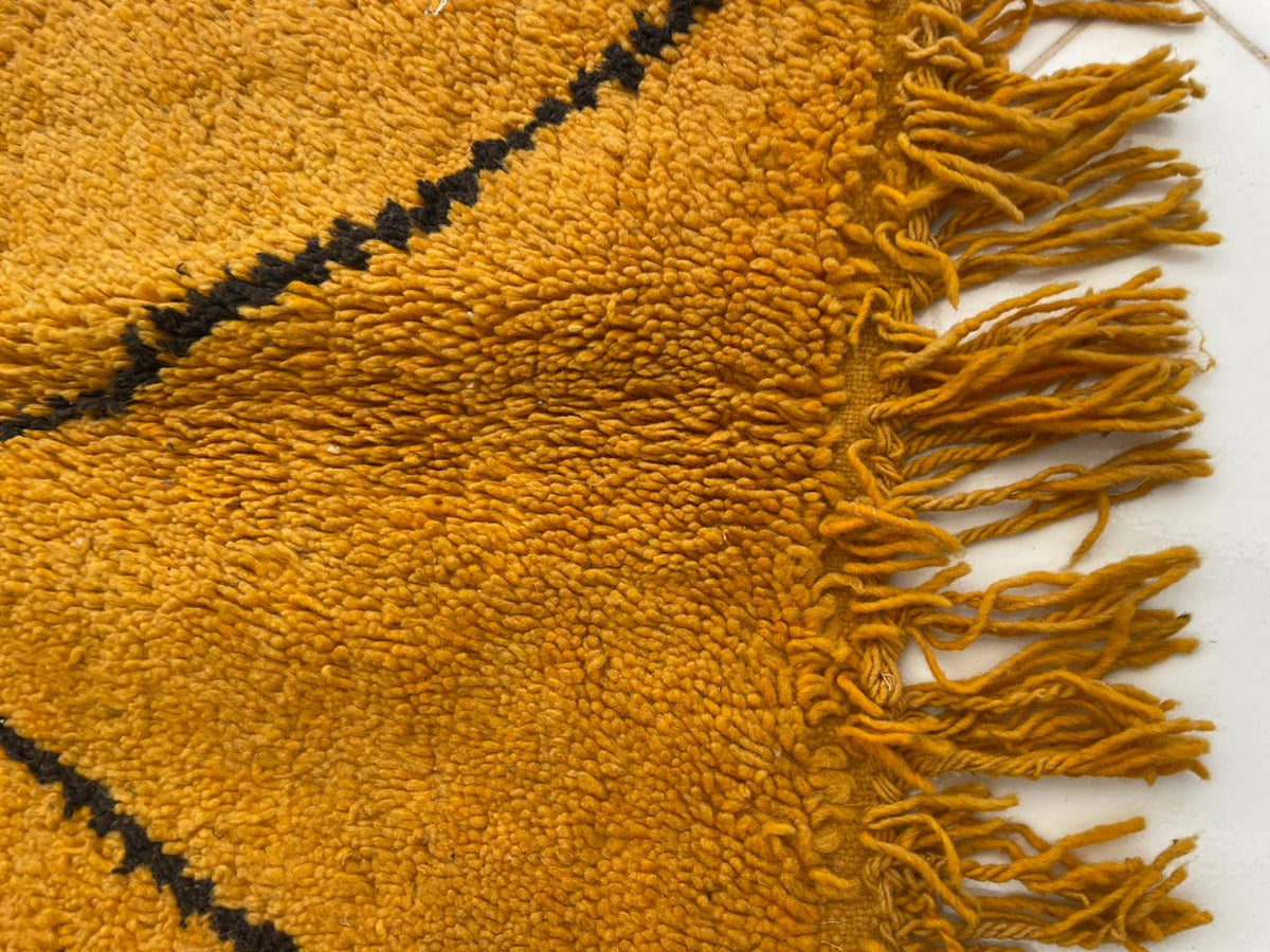 Detail view of a yellow wool rug showcasing fringe edges and a textured surface.