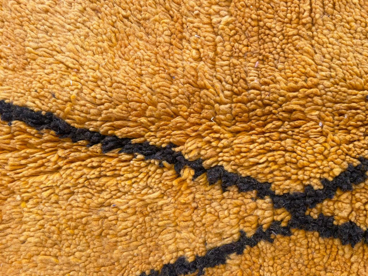 Detail shot of a yellow wool rug with a geometric pattern and smooth surface.