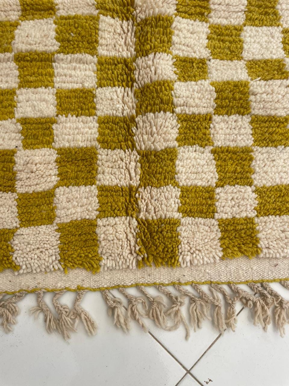Detail shot of a yellow and cream rug showcasing fringe detail and a checkered pattern.