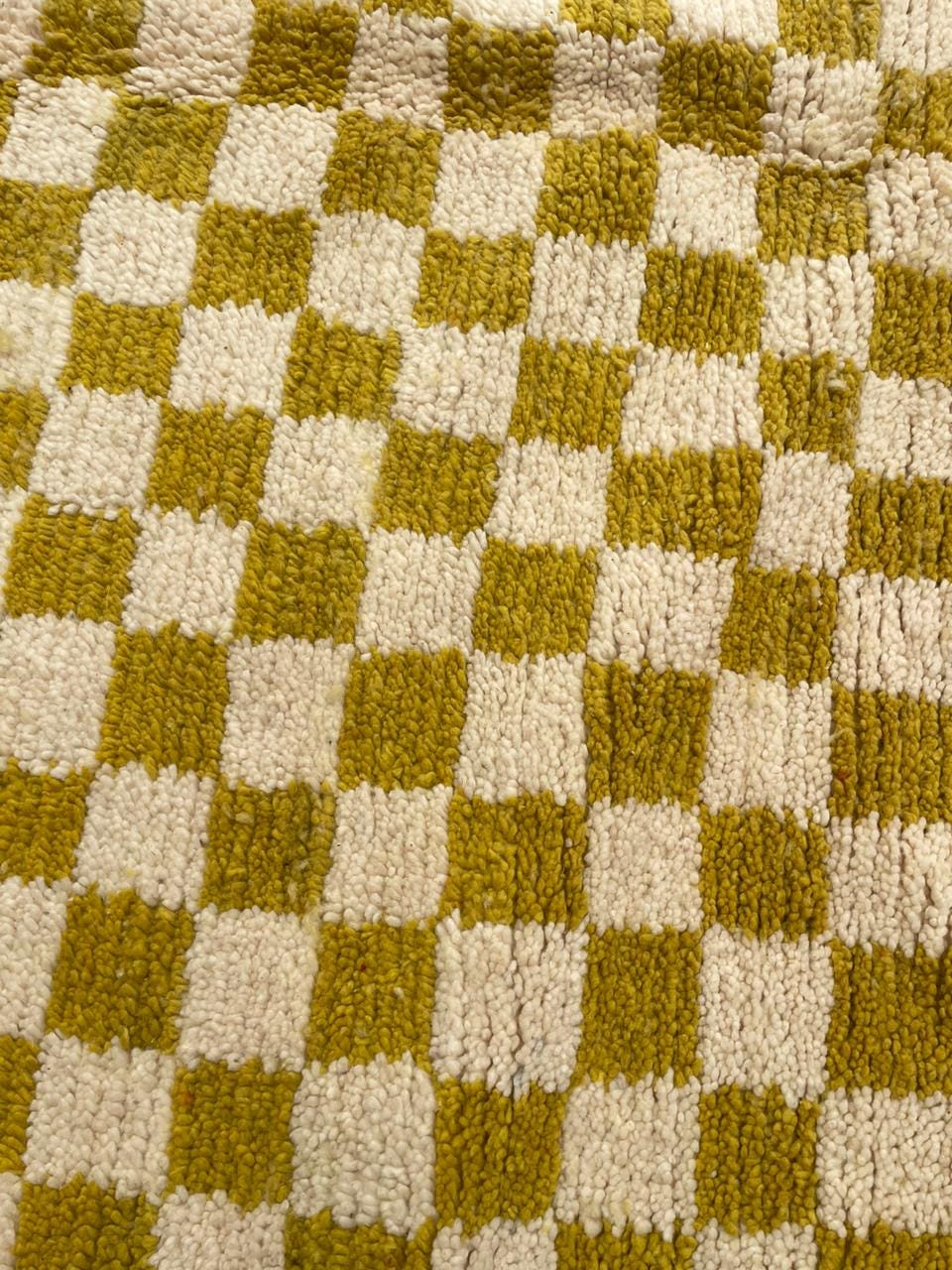 Detail shot of a yellow and cream rug featuring a checkered pattern and soft texture.