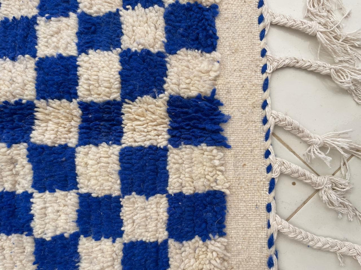 Detail shot of a checkered wool rug with fringe edges against a white background.