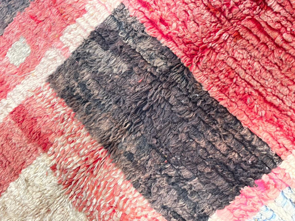 Close-up of a faded red Moroccan rug highlighting tribal patterns and textures.