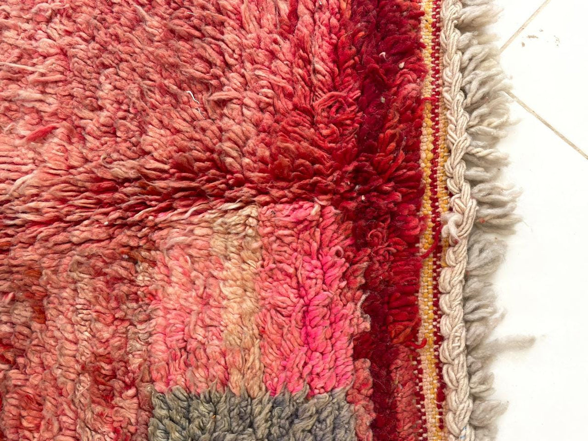 Detail view of a faded red Boujaad rug with tribal patterns and fringe edges.