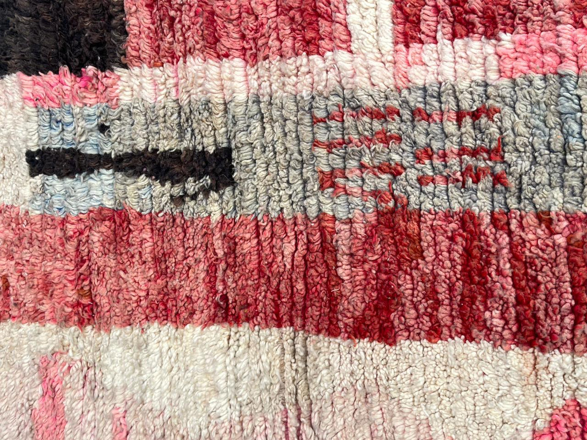 Detailed view of a faded red Moroccan rug with tribal patterns and black accents.