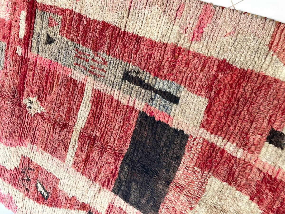 Detail view of a faded red Moroccan rug showcasing artistic tribal patterns.
