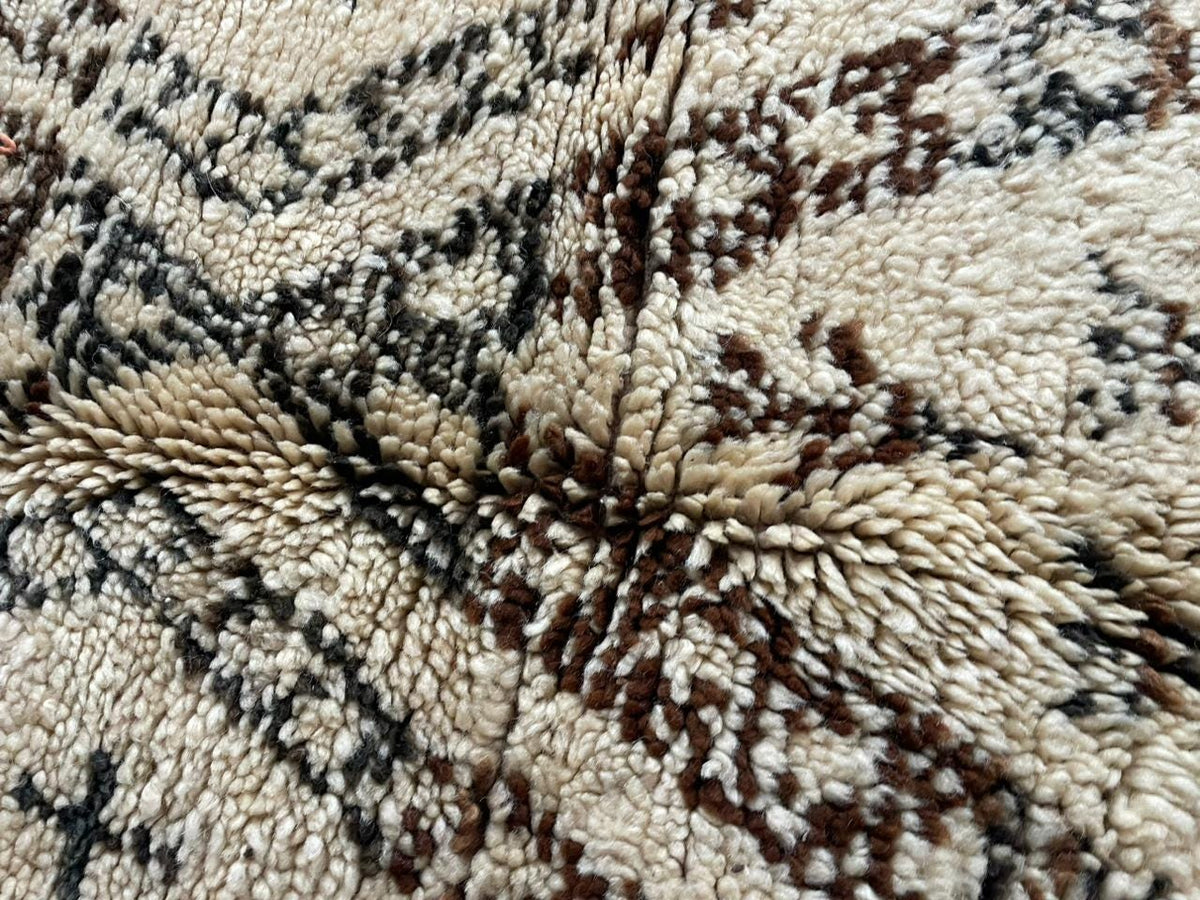 Detail close-up of a vintage Moroccan rug in beige and black with geometric patterns and a textured surface.