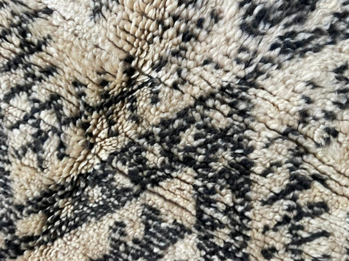 Top view of a beige and black Moroccan rug showcasing geometric patterns and fringe edges.