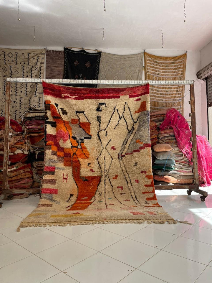 Lifestyle shot of a vintage Moroccan rug with tribal patterns in beige, orange, and red.