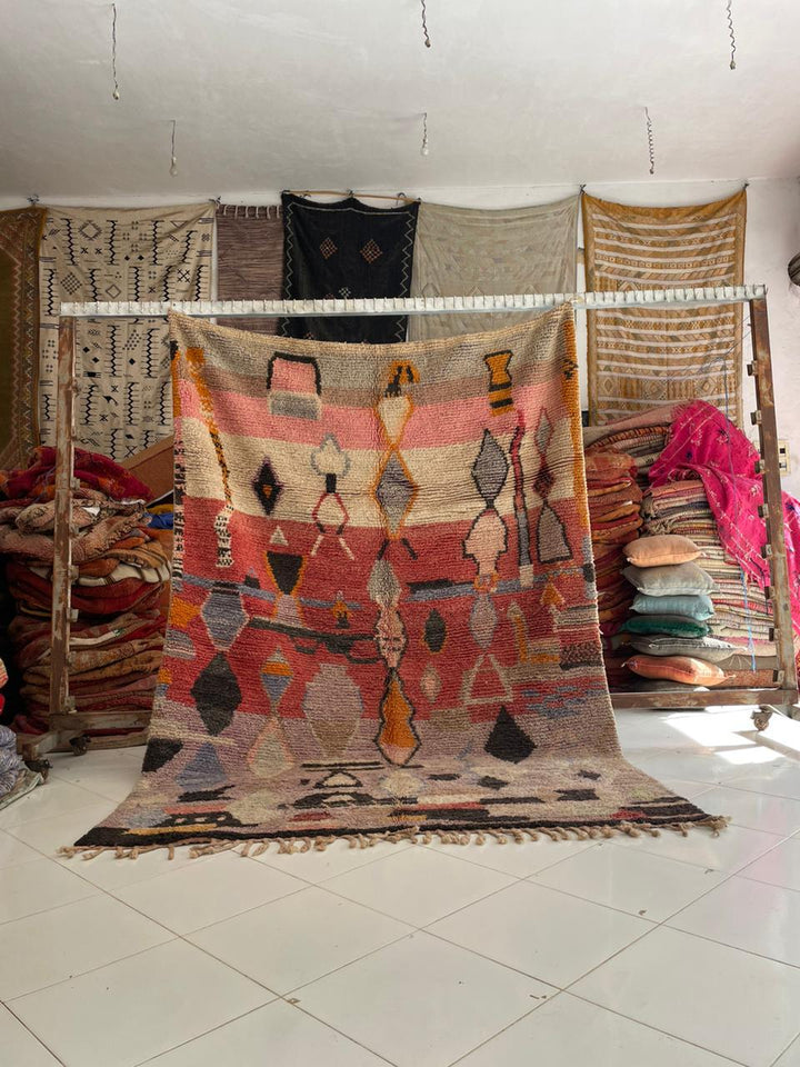 Lifestyle shot of a red and orange tribal rug with fringe edges on a natural background.