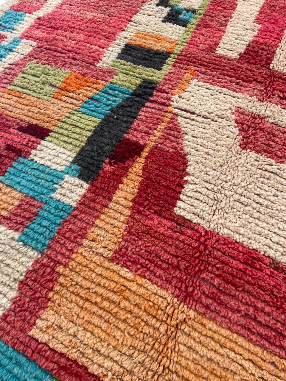 Close-up detail of a vintage Moroccan rug featuring tribal patterns in red, blue, and cream.