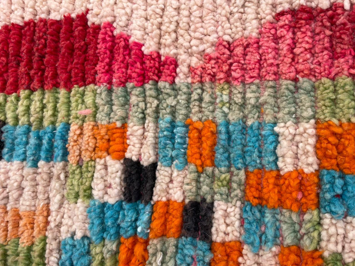 Close-up detail of a vintage Moroccan rug showcasing tribal patterns in pink, green, and blue.