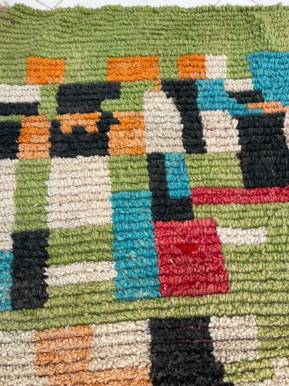 Close-up detail of a vintage Moroccan rug featuring tribal patterns in green, black, and orange.