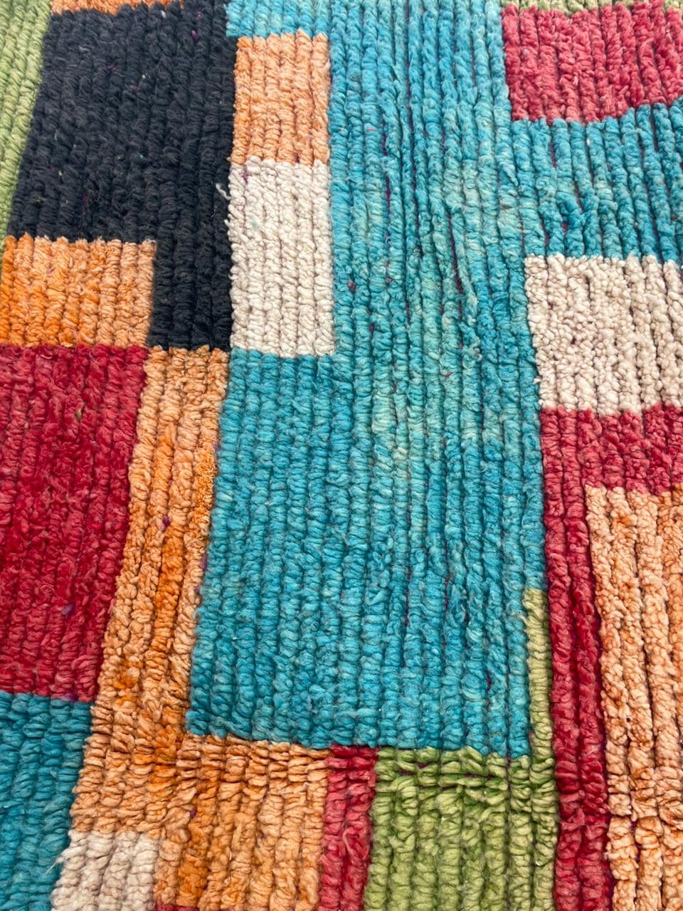 Close-up detail of a vintage Moroccan rug with tribal patterns in red, blue, and orange.