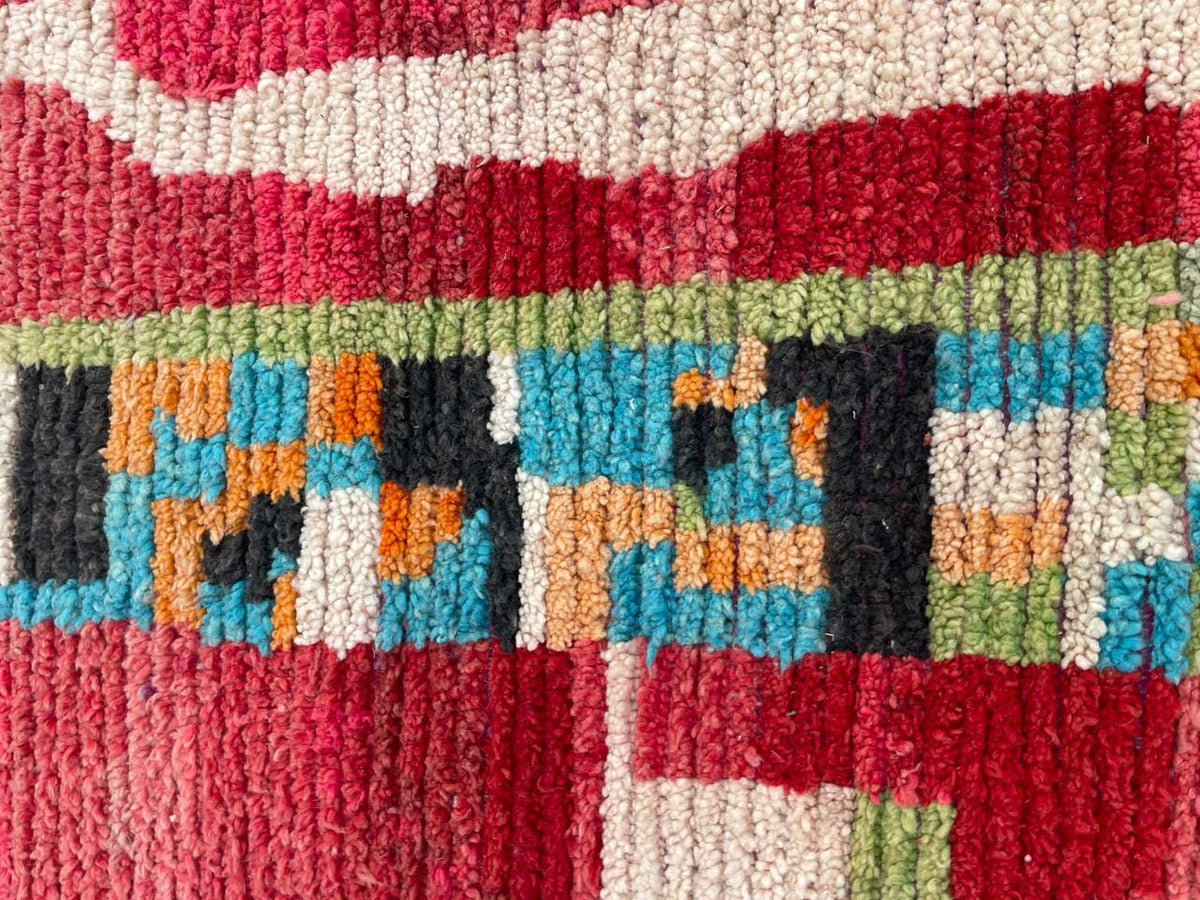Close-up detail of a vintage Moroccan rug featuring vibrant tribal patterns in red, black, and green.