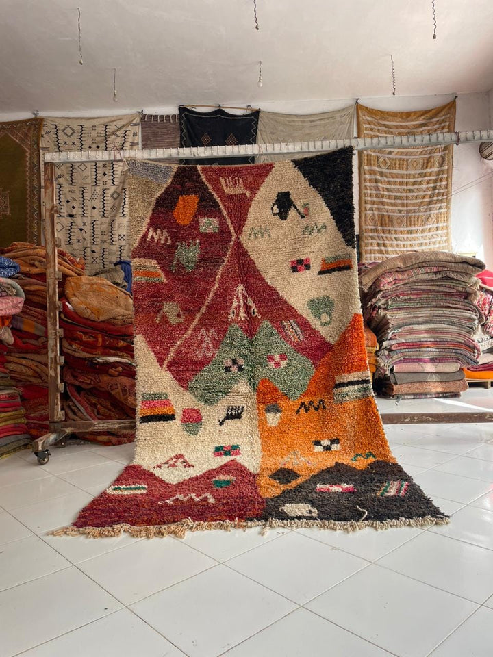 Lifestyle shot of a vintage Moroccan rug featuring geometric patterns in red, orange, and green.