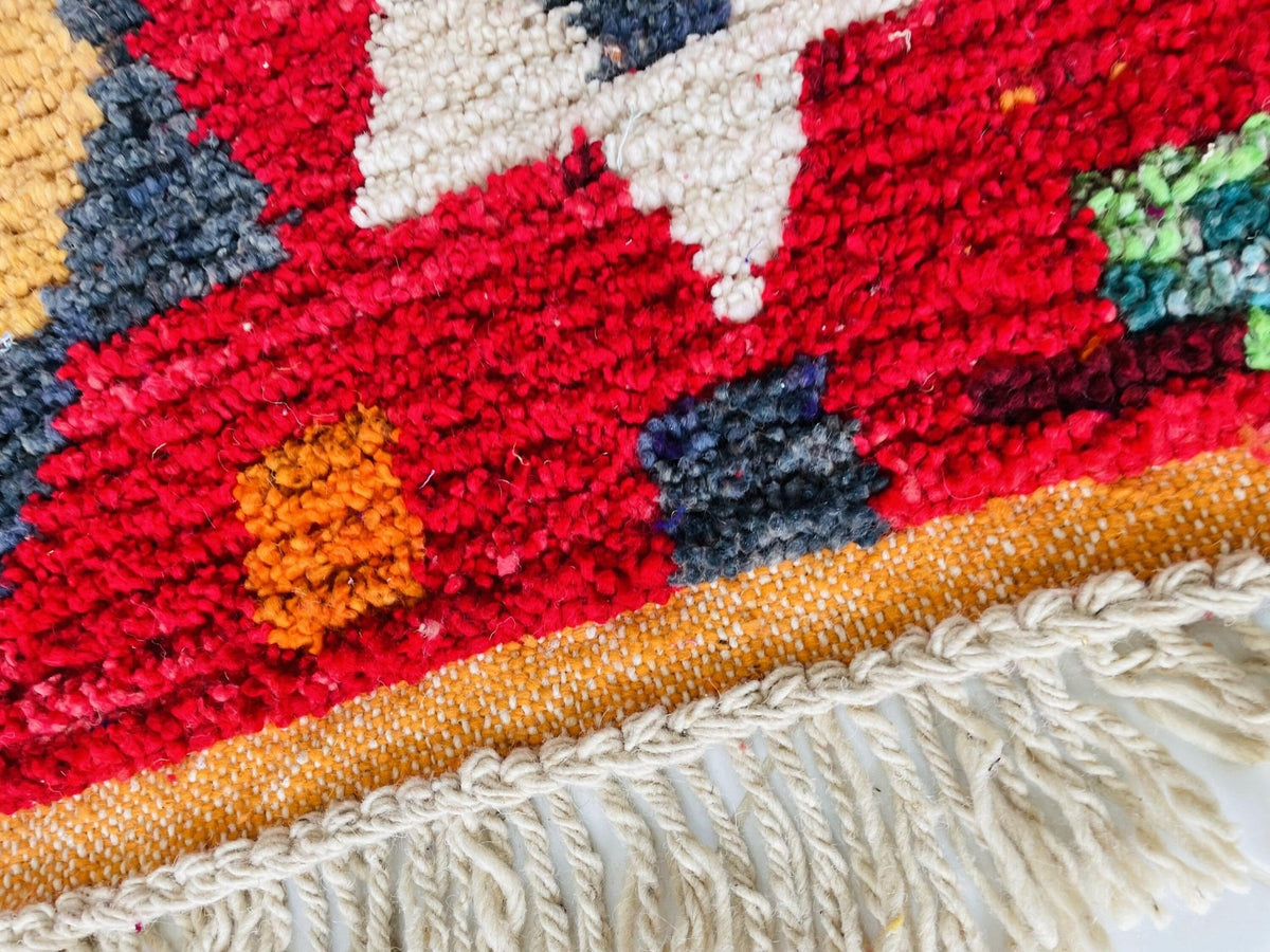 Detail shot of the edge of a red vintage Boujaad Moroccan rug showcasing fringe and colorful patterns.