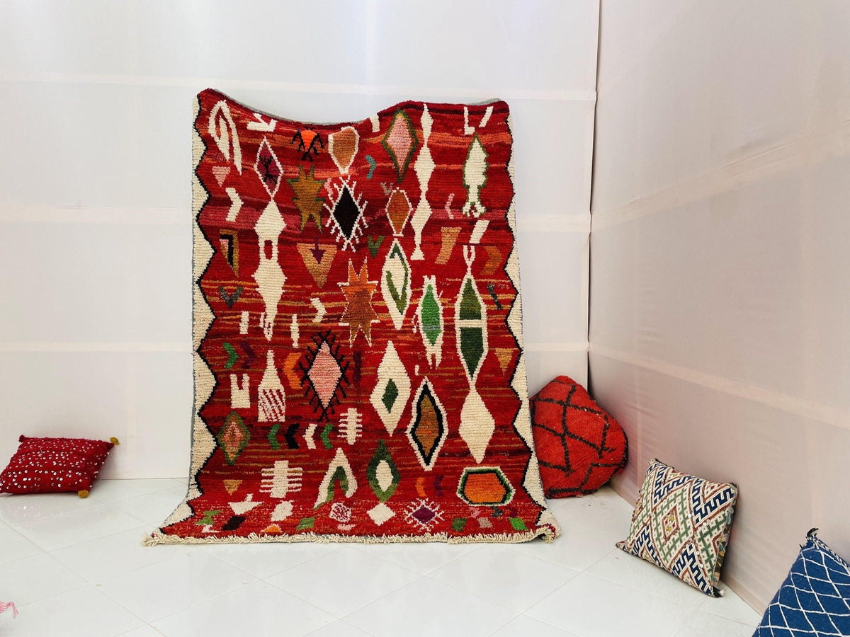 Lifestyle shot of a red vintage Moroccan rug with tribal patterns on a white background.
